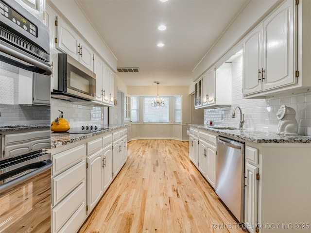 5610 S 75th E Pl, Tulsa, OK 74145 - kitchen with stainless steel appliances, a chandelier, white cabinetry, light wood finished floors, and backsplash