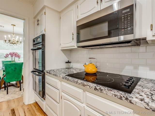 5610 S 75th E Pl, Tulsa, OK 74145 - kitchen with black appliances, a chandelier, light wood-type flooring, backsplash, and white cabinets