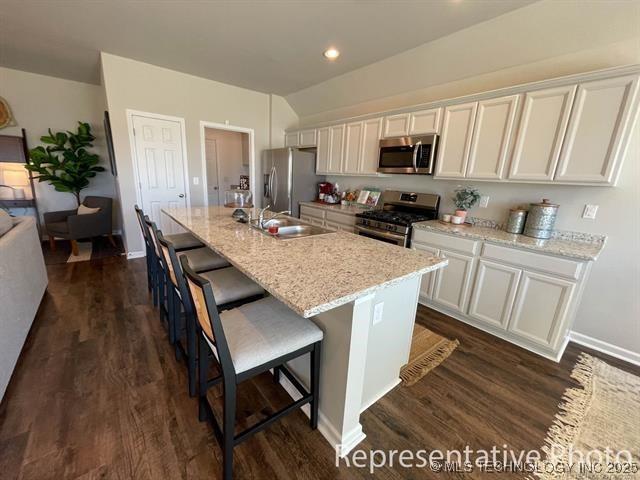 8308 E Oakland St, Broken Arrow, OK 74014 - kitchen featuring appliances with stainless steel finishes, dark wood-type flooring, a kitchen island with sink, white cabinets, and a breakfast bar