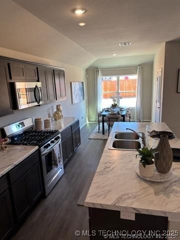 8308 E Oakland St, Broken Arrow, OK 74014 - kitchen with appliances with stainless steel finishes, a kitchen island with sink, dark wood-style flooring, lofted ceiling, and recessed lighting