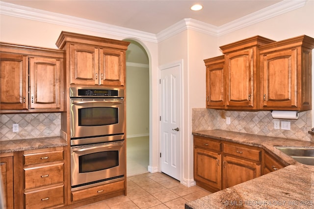 1004 E Fargo St S, Broken Arrow, OK 74012 - kitchen featuring double oven, backsplash, brown cabinetry, light tile patterned floors, and crown molding