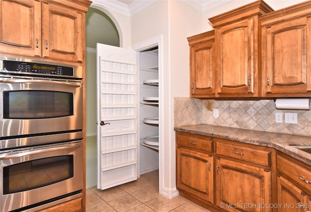 1004 E Fargo St S, Broken Arrow, OK 74012 - kitchen featuring double oven, crown molding, decorative backsplash, light tile patterned floors, and dark stone countertops