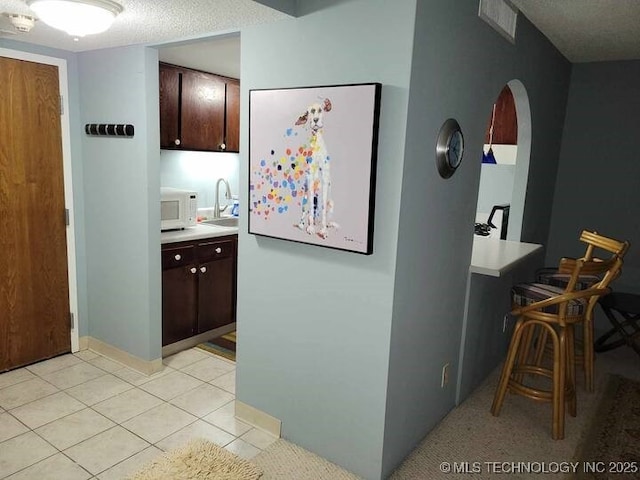 450 W 7th St Unit 704, Tulsa, OK 74119 - kitchen with dark brown cabinetry, light countertops, white microwave, and light tile patterned floors