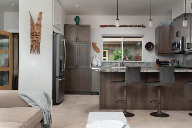 kitchen with a breakfast bar area, dark brown cabinets, decorative light fixtures, and appliances with stainless steel finishes