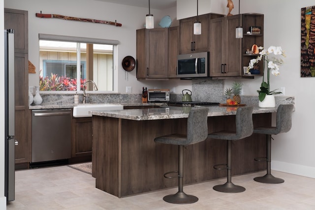 kitchen with dark brown cabinetry, sink, stainless steel appliances, light stone counters, and pendant lighting