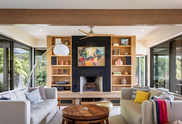 living room with a tiled fireplace, ceiling fan, and a healthy amount of sunlight