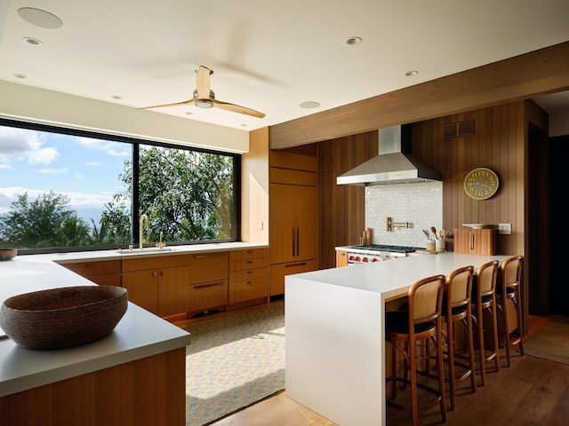 kitchen with ceiling fan, sink, wall chimney exhaust hood, a kitchen breakfast bar, and range