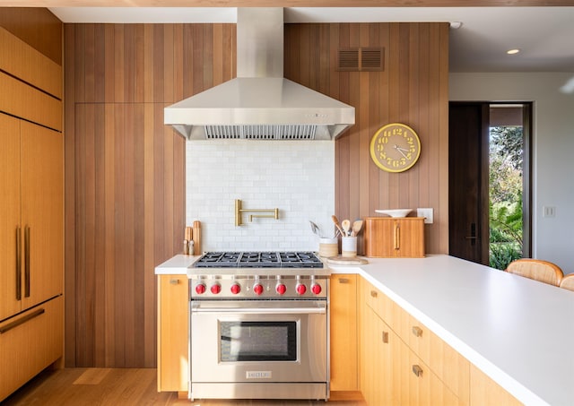 kitchen with wall chimney exhaust hood, premium stove, light hardwood / wood-style floors, and backsplash