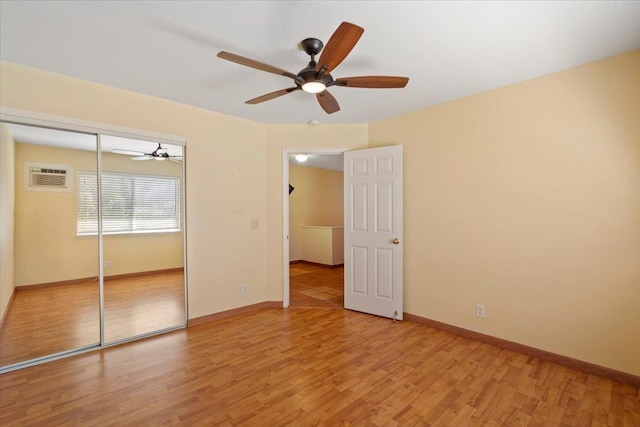 unfurnished bedroom with light wood-style flooring, a wall mounted AC, and baseboards