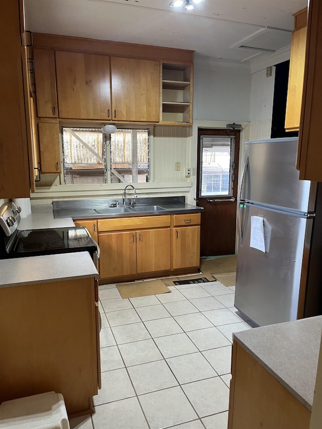 kitchen with a sink, range with electric stovetop, freestanding refrigerator, light tile patterned flooring, and brown cabinetry