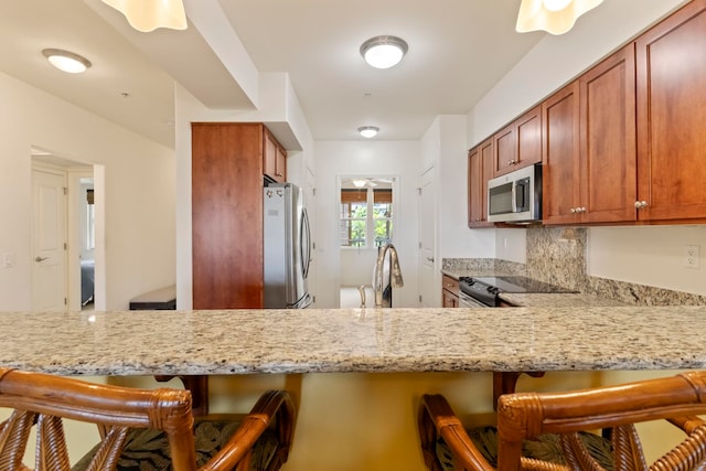 28 Hauwahine Ln Unit F203, Kihei, HI 96753 - kitchen featuring appliances with stainless steel finishes, a kitchen bar, light stone countertops, and brown cabinets