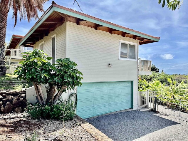 view of home's exterior with a garage, fence, asphalt driveway, and a balcony