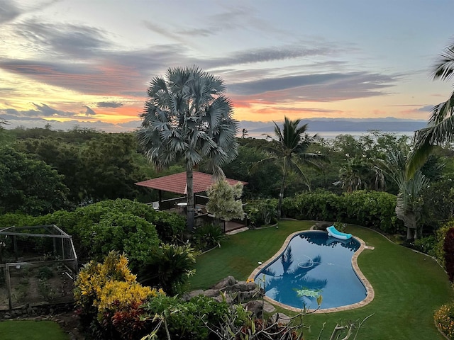 pool at dusk featuring a lawn