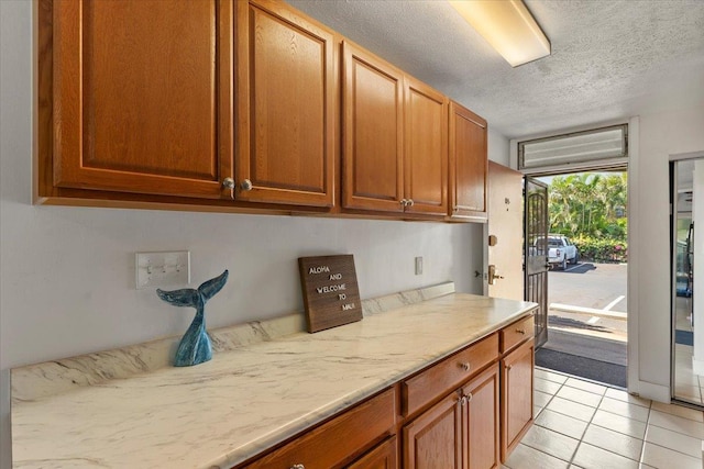 kitchen with a textured ceiling, light tile patterned floors, and light stone counters