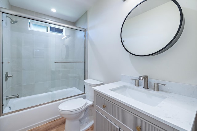 full bathroom featuring vanity, hardwood / wood-style flooring, enclosed tub / shower combo, and toilet