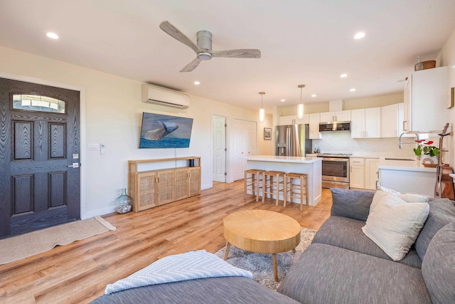 living room featuring ceiling fan, sink, a wall mounted air conditioner, and light wood-type flooring