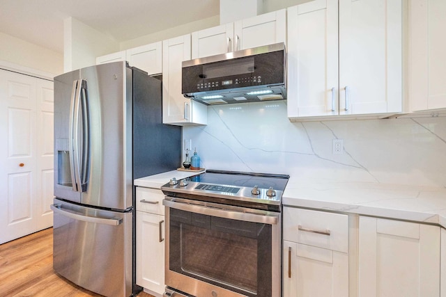 kitchen with white cabinetry, light stone counters, light hardwood / wood-style flooring, appliances with stainless steel finishes, and exhaust hood