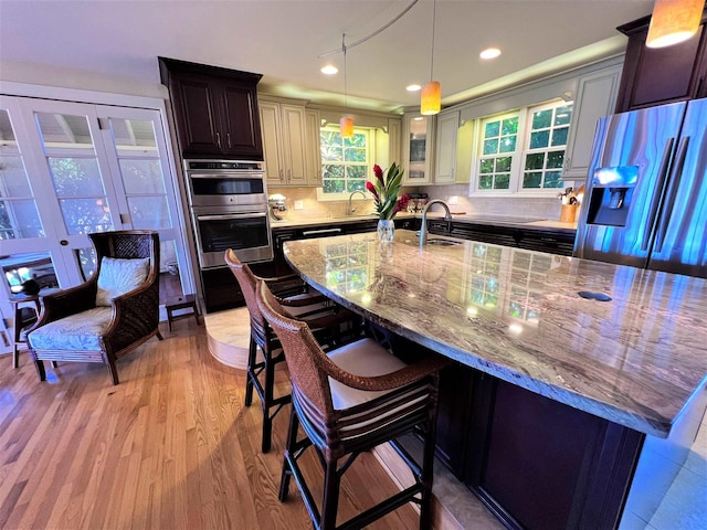 kitchen featuring pendant lighting, stainless steel appliances, sink, light wood-type flooring, and a breakfast bar area