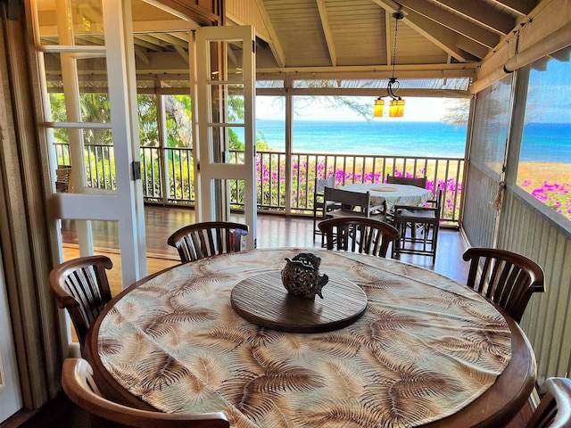 dining space with a water view, lofted ceiling with beams, a view of the beach, and wood-type flooring