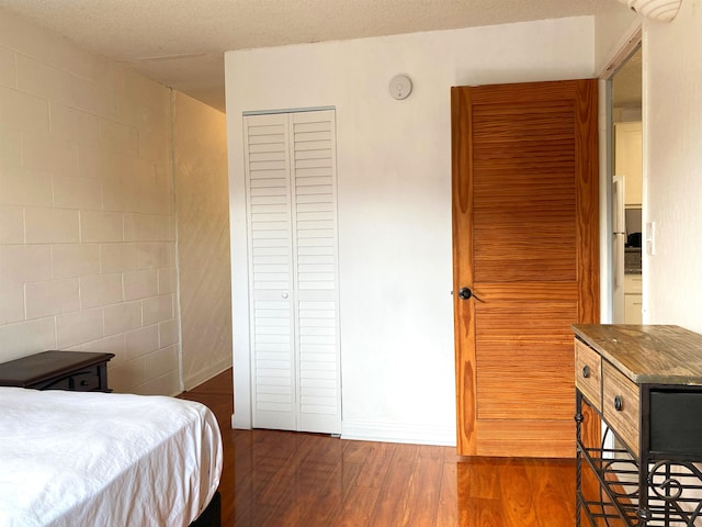 bedroom with dark hardwood / wood-style flooring, tile walls, a textured ceiling, and a closet