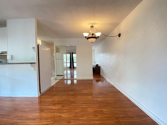 unfurnished dining area featuring wood-type flooring, a textured ceiling, and a notable chandelier