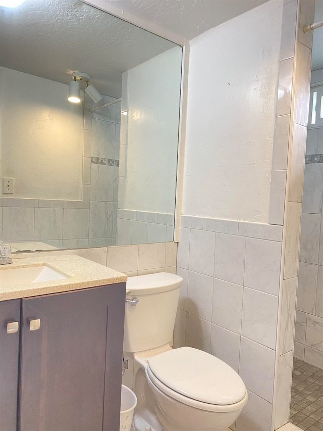 bathroom with vanity, toilet, a textured ceiling, tile walls, and a tile shower