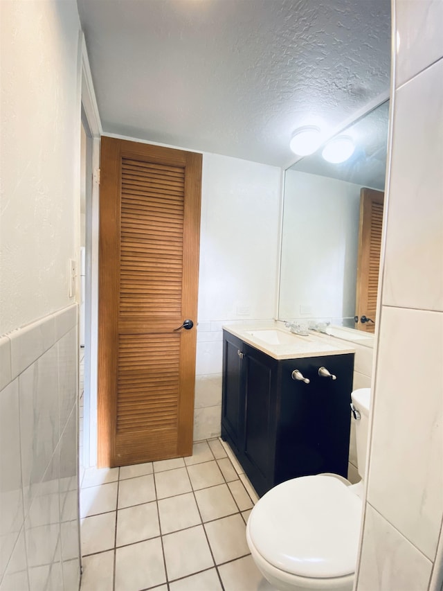 bathroom featuring tile patterned floors, vanity, a textured ceiling, tile walls, and toilet