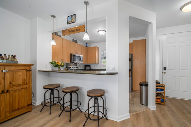 kitchen with a breakfast bar area, light hardwood / wood-style flooring, kitchen peninsula, and pendant lighting