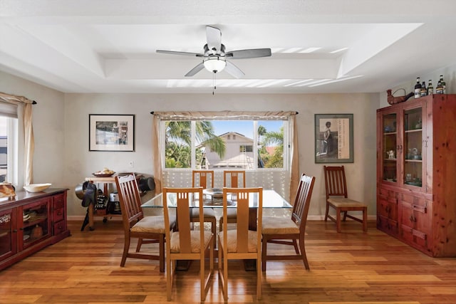 dining space with baseboards, a raised ceiling, light wood-style floors, and ceiling fan