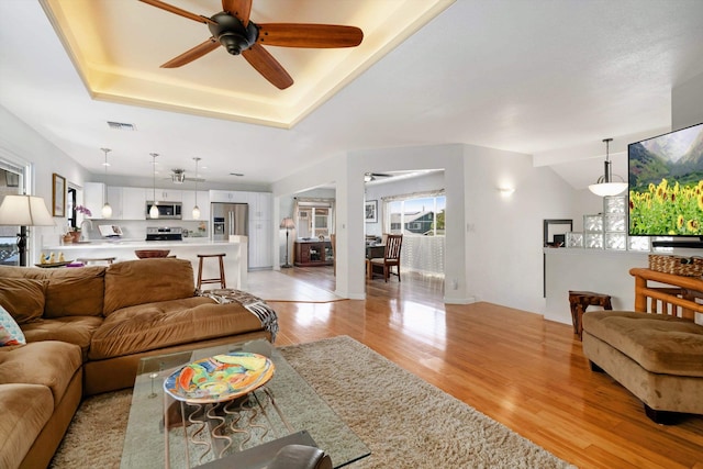 living room with a tray ceiling, light wood-style flooring, a healthy amount of sunlight, and visible vents