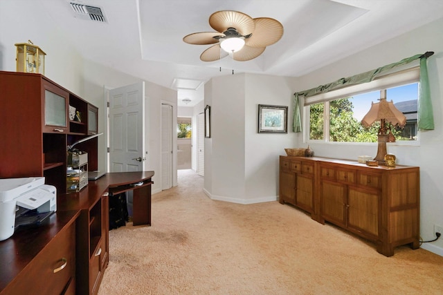 office space featuring a tray ceiling, light colored carpet, visible vents, and baseboards