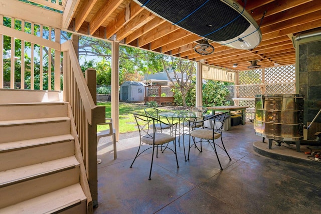 view of patio with a storage unit, fence, an outdoor structure, outdoor dining area, and stairs