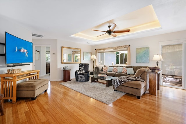 living area with light wood-type flooring, a raised ceiling, and visible vents