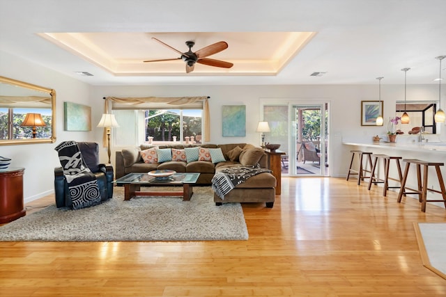 living area with visible vents, light wood-type flooring, and a tray ceiling