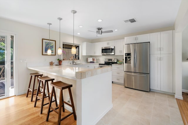 kitchen featuring visible vents, a sink, appliances with stainless steel finishes, a breakfast bar area, and a peninsula