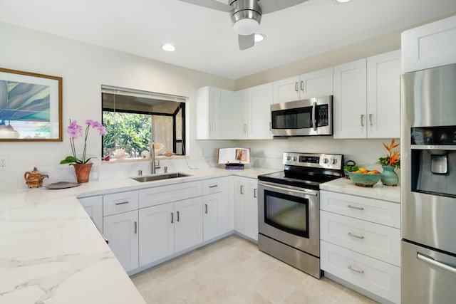 kitchen with light stone countertops, appliances with stainless steel finishes, white cabinets, a ceiling fan, and a sink