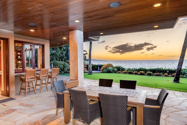 patio terrace at dusk featuring a lawn and a water view