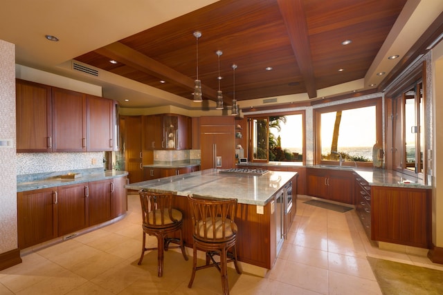 kitchen with beamed ceiling, a center island, built in appliances, light stone counters, and a raised ceiling