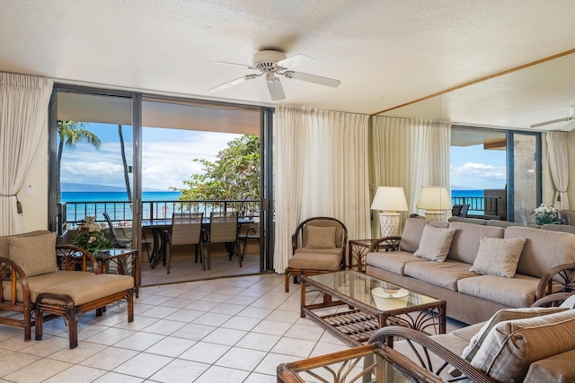 tiled living room with ceiling fan, a textured ceiling, a wall of windows, and a water view