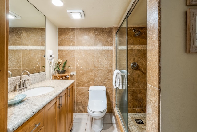 bathroom with tile walls, vanity, tile patterned flooring, a shower with door, and toilet