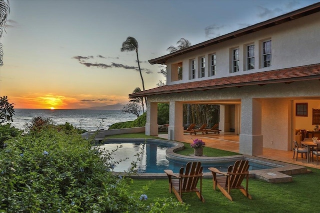 back house at dusk with a water view, a patio area, and a yard