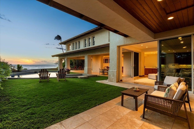 back house at dusk with a water view, a yard, and a patio area