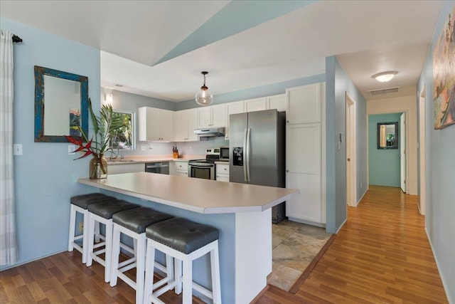 kitchen featuring kitchen peninsula, white cabinetry, hanging light fixtures, appliances with stainless steel finishes, and a kitchen breakfast bar