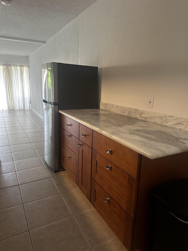 715 S Kihei Rd Unit D143, Kihei, HI 96753 - kitchen with freestanding refrigerator, a textured ceiling, dark tile patterned floors, light countertops, and brown cabinetry