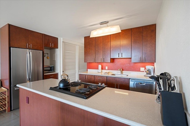 kitchen featuring appliances with stainless steel finishes, a sink, light countertops, and a peninsula