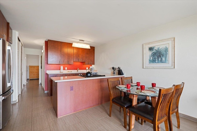 kitchen with freestanding refrigerator, a peninsula, light countertops, brown cabinets, and black gas cooktop