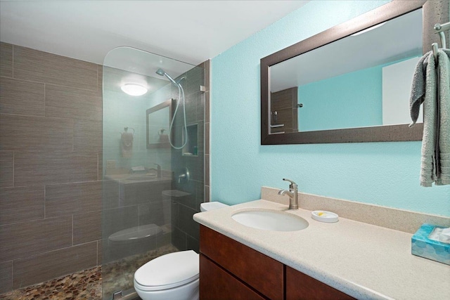 bathroom with toilet, a walk in shower, vanity, and a textured wall