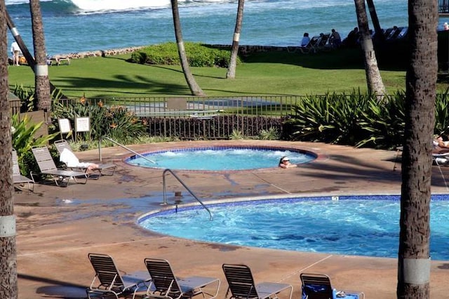 view of swimming pool with a community hot tub, fence, a pool, a patio area, and a water view
