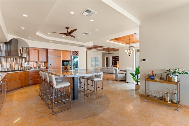 kitchen featuring a large island, a kitchen breakfast bar, a raised ceiling, extractor fan, and ceiling fan with notable chandelier