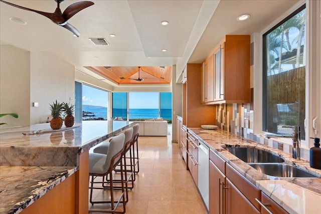 kitchen with sink, a kitchen breakfast bar, light stone counters, stainless steel dishwasher, and a water view